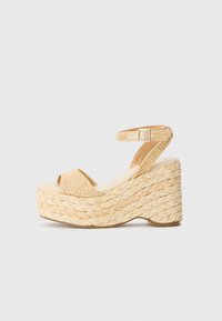 Sandalias de cuña de plataforma con exterior de paja trenzada, color beige, diseño de punta abierta y una delgada correa en el tobillo asegurada con una hebilla.