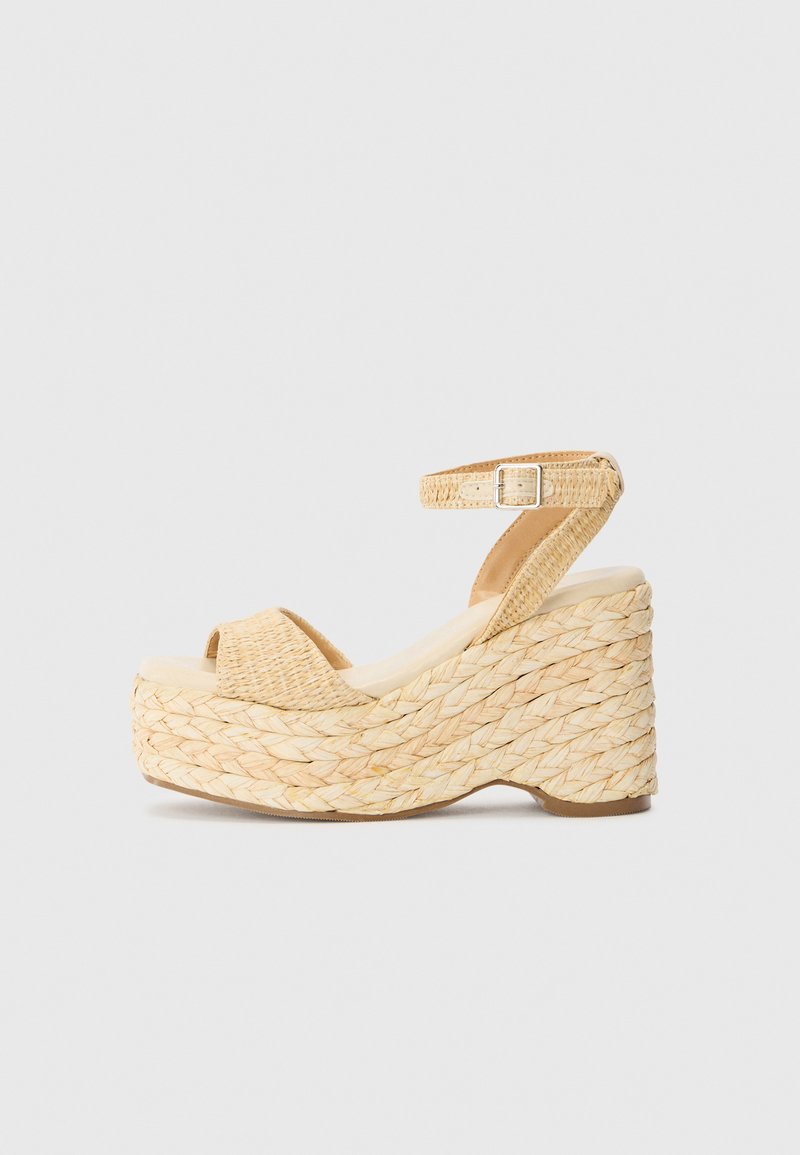 Sandalias de cuña de plataforma con exterior de paja trenzada, color beige, diseño de punta abierta y una delgada correa en el tobillo asegurada con una hebilla.