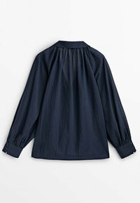 Granatowa bluzka z długim rękawem, z marszczonym karczkiem, zapinanymi na guziki mankietami i luźnym, zwiewnym krojem, widoczna od tyłu na białym tle.