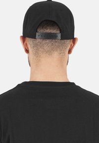 Schwarze Snapback-Cap von hinten betrachtet, mit flachem Schirm, verstellbarem Plastikverschluss und strukturiertem Stoff.