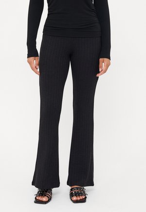 Pantalons évasés noir à côtes avec un motif texturé, associés à des sandales noires à lanières ornées d'accents circulaires. Tissu lisse et extensible.