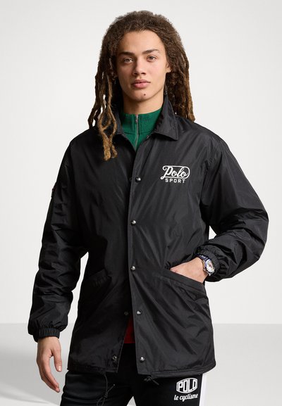 Schwarze Windbreaker-Jacke mit Druckknopf-Leiste, elastischen Bündchen und einem "Polo Sport"-Logo auf der linken Brust. Strukturierter Stoff mit Taschen.