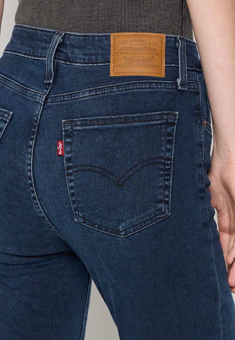 Dunkelblaue Jeans aus Denim mit hoher Taille, dezenten Nähdetails, einem braunen Leder-Logo-Patch und einem kleinen roten Etikett an der hinteren Tasche.