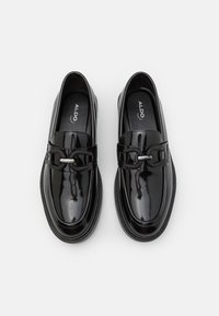 Mocassins en cuir verni noir avec une finition lisse, dotés d'un détail en chaîne sur la sangle, d'un bout arrondi et d'une semelle extérieure en caoutchouc texturé.