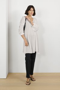Lichtgrijze tuniek van textuurstof, met geplooid ontwerp en driekwartmouwen, gecombineerd met zwarte tapered broek en zwarte teenslippers.