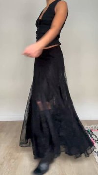 Person iført en ærmeløs sort top og et flydende sort blonder nederdel, der drejer rundt indendørs på et lyst trægulv.