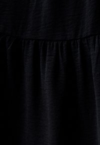 Black fabric with a wrinkled texture, featuring gathered detailing at the seam. The material appears soft and loosely woven.