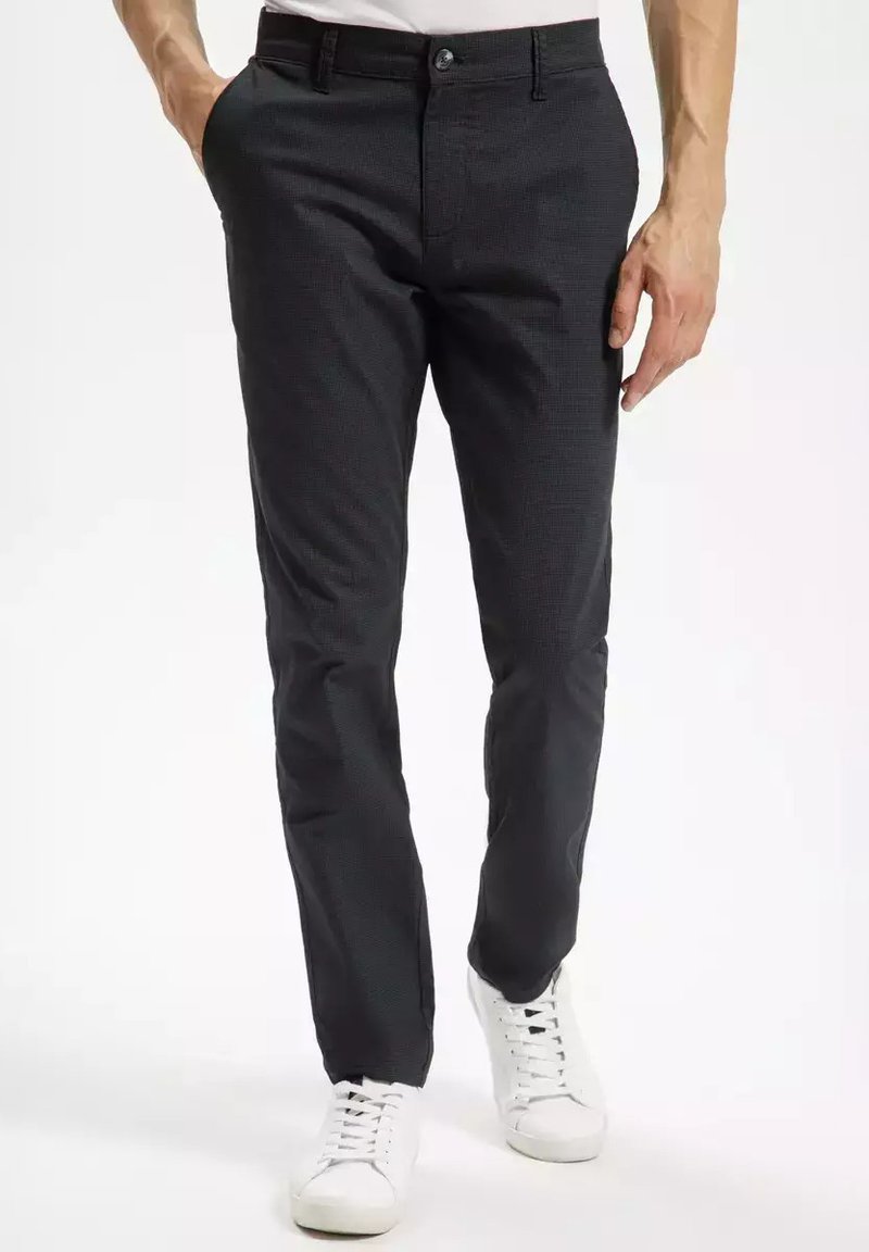 Ciemnoszare spodnie z delikatną fakturą, dopasowane, z przednimi kieszeniami, w połączeniu z białymi sneakersami. Posiadają zapięcie na guzik oraz szlufki na pasek.