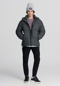 Kurtka puchowa w ciemnoszarym kolorze, z zamkiem z przodu, kapturem i teksturowanym materiałem. Połączona z czarnymi spodniami cargo i wzorzystymi sneakersami.