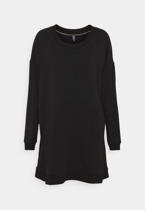 Robe sweat-shirt noire à manches longues et coupe oversize, col rond côtelé, poignets, ourlet et fentes latérales sur un fond clair uni.