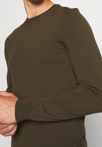 Olivgrüner, langärmeliger Rundhalspullover aus geripptem Strickstoff, mit taillierter Form und subtiler Textur, samt enganliegenden Bündchen.