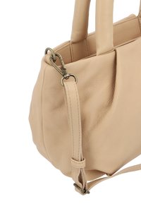 Beżowa skórzana torebka w rogu z podwójnymi uchwytami i odpinanym paskiem przymocowanym mosiężnym obrotowym zapięciem.