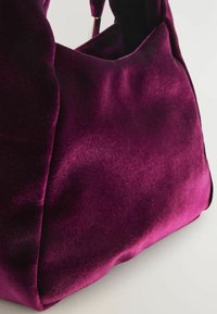 Geantă mov din catifea, cu textură moale și formă rotunjită. Include cusături vizibile și o mică deschidere în partea de sus.