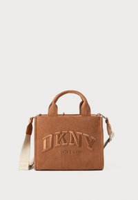 Pruunist korgist DKNY kott pehmeate käepidemetega, tikandiga logo ja eemaldatava beeži õlarihmaga, valge ühtlase tausta ees.