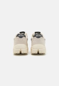 Beige sneakers with a suede upper and mesh accents. Features a thick, textured sole and branded heel tab in dark blue.