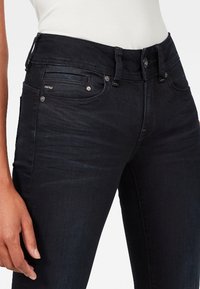 Höga mörka denimjeans med slim fit. Har framfickor, metallknapp och sömnadsdetaljer. Slät textur med lätt glans.