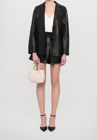 Zwarte leren blazer over een wit topje, gecombineerd met zwarte leren shorts, een lichtgekleurde handtas en zwarte hoge hakken.