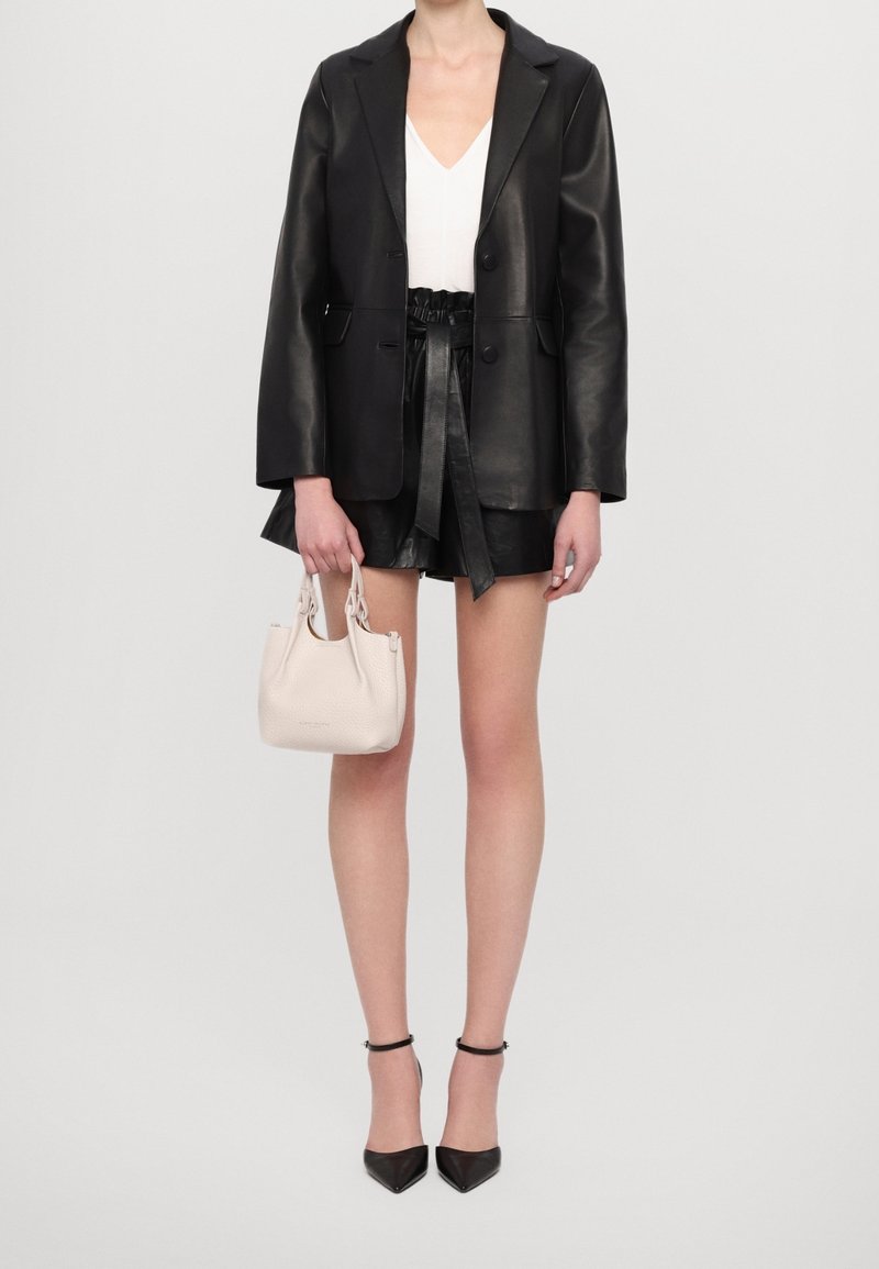 Zwarte leren blazer over een wit topje, gecombineerd met zwarte leren shorts, een lichtgekleurde handtas en zwarte hoge hakken.