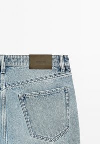 Jean en denim bleu clair vue de dos avec une poche unique et une étiquette de marque en cuir marron portant l'inscription Massimo Dutti sur la ceinture.