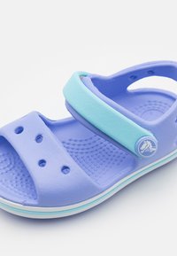 Purple sandal with a light blue strap, textured upper, and drainage holes; features a round frog logo on the strap, white sole accent.