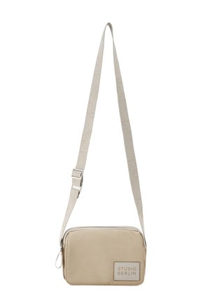 Kleine beige rechteckige Umhängetasche mit verstellbarem Riemen, der auf dem vorderen Aufnäher und dem Riemen den Schriftzug „Studio Berlin“ trägt.
