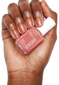 Bouteille de vernis à ongles avec un capuchon blanc et une formule de gelée rose. Une main montre des ongles naturels peints dans une teinte nude assortie.