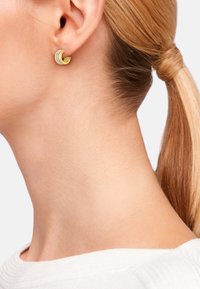 Pendientes de tono dorado con formas de media luna en capas y pequeñas piedras transparentes. La textura aplicada añade dimensión; se llevan en una oreja perforada.