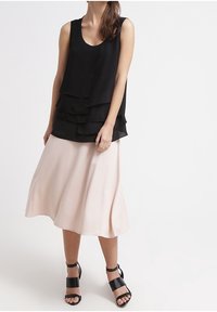 Černý vrstvený top bez rukávů, růžová midi sukně a černé sandály na blokovém podpatku se zapínáním na pásky. Měkká tkanina, splývavý design a hladká textura.