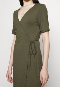 Robe portefeuille en vert olive, à manches courtes, en tissu doux et extensible. Dotée d'un décolleté en V et d'une fermeture par lien à la taille pour un ajustement réglable.