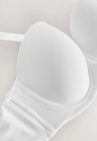 Reggiseno bianco imbottito con tessuto liscio, supporto con ferretto e spalline regolabili. Presenta un design senza cuciture e una texture morbida.