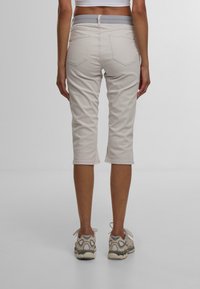 Beige Capri-Hosen aus einem strukturierten Stoff mit elastischem Bund. Sie verfügen über zwei Gesäßtaschen und haben eine schmale Passform, die knapp unter dem Knie endet.