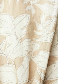 Tissu beige et blanc avec un contour abstrait de grandes feuilles tropicales superposées, créant un motif doux et naturel.