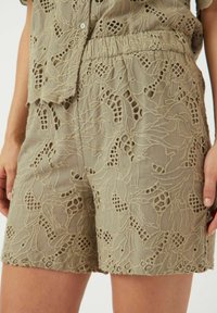 Linshorts i lys beige med intrikate broderier, som har utskårne blomsterdesign og en elastisk midje for komfort.