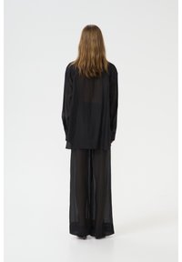 Blouse noire transparente et pantalon large, tissu léger, coupe ample, manches longues et transparence partielle. Pas de motifs ou de matériel visibles.