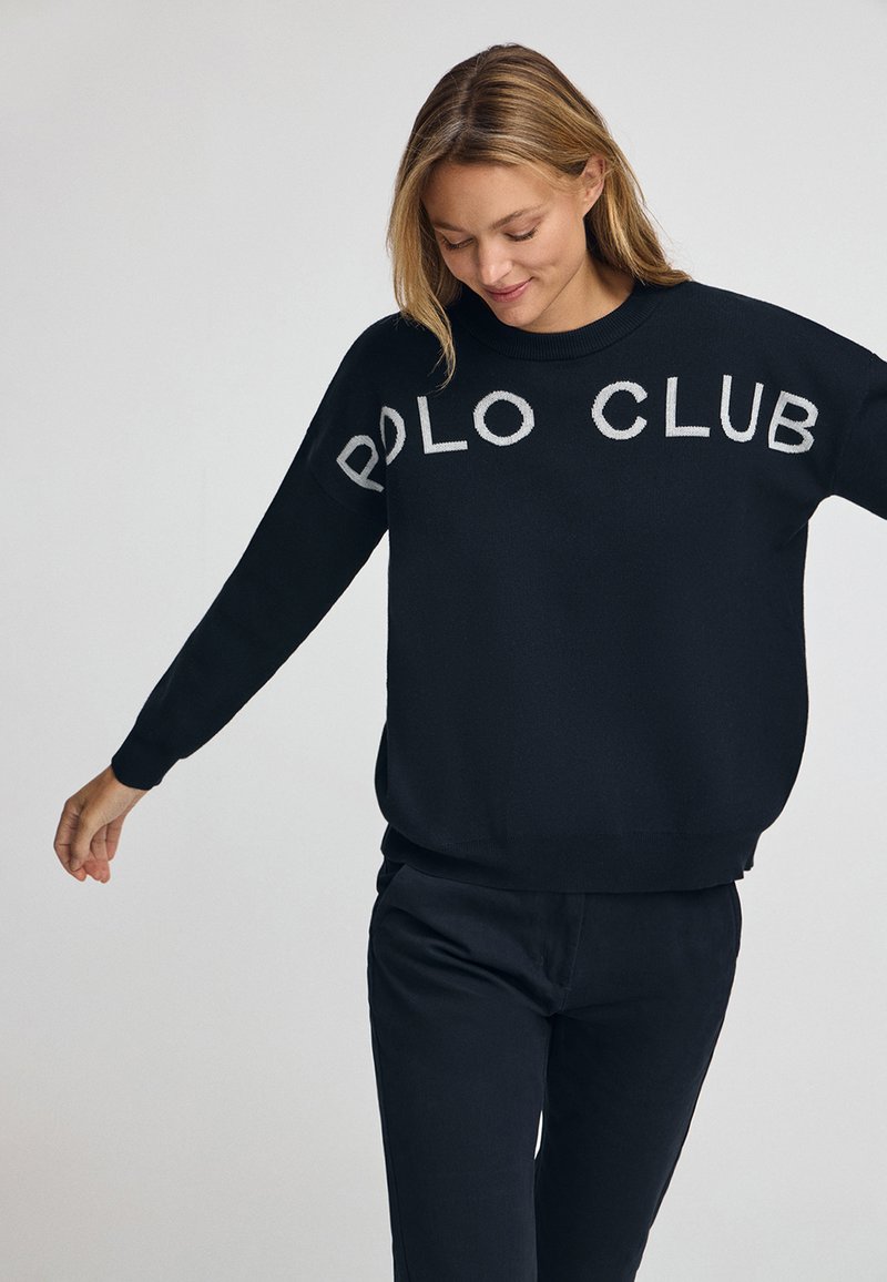 Svart stickad tröja med "POLO CLUB" broderat i ljusgrått över bröstet; avslappnad passform, rund halsringning, långa ärmar, mjukt tyg.