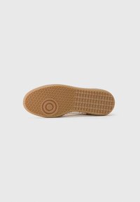 Rubber-soled sneaker with a textured, gum outsole. Features a geometric pattern and rounded accents. Color is predominantly light with neutral tones.