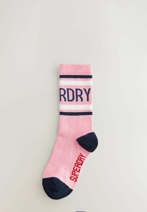Rožinės kojinės su mėlynomis juostelėmis ir navy spalvos tekstu "SUPERDRY". Pirštas ir kulnas yra tamsiai mėlynos spalvos, su lygiu paviršiumi.