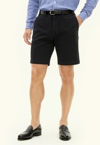 Czarne bawełniane szorty o regularnym kroju, z bocznymi kieszeniami i mankietami, noszone z niebieską koszulą w paski i czarnymi mokasynami.