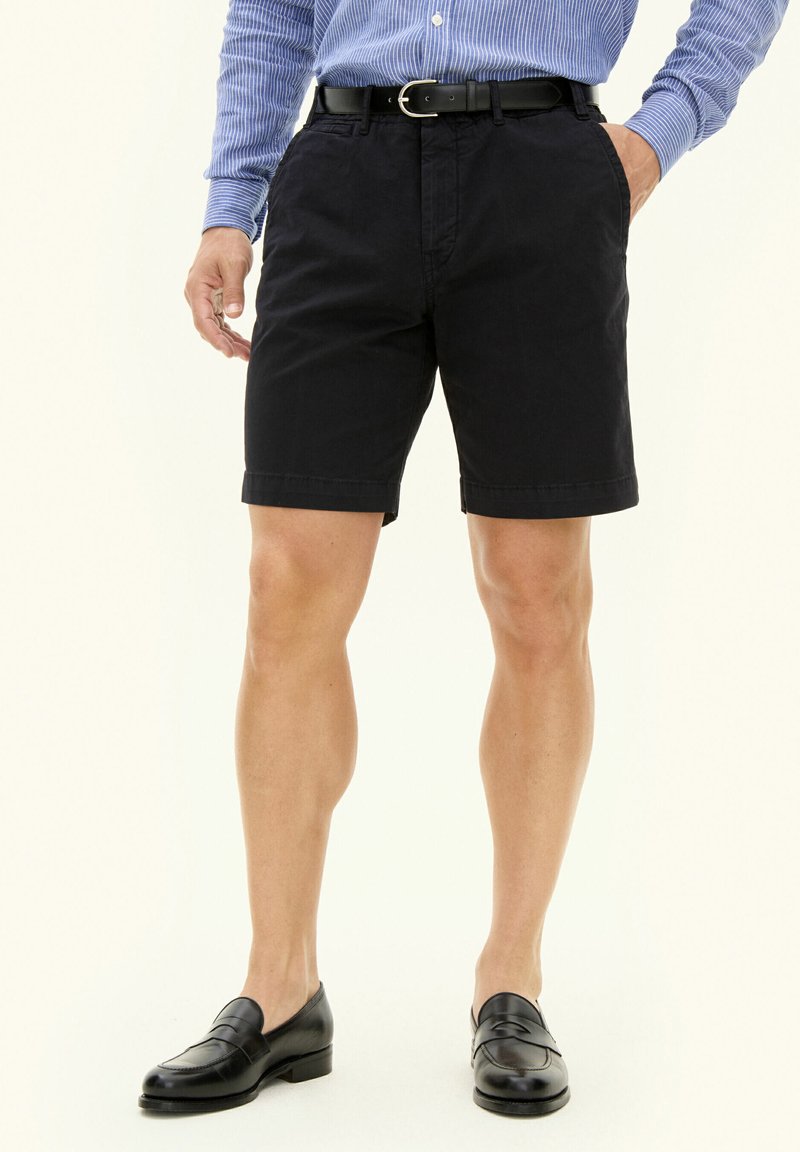 Czarne bawełniane szorty o regularnym kroju, z bocznymi kieszeniami i mankietami, noszone z niebieską koszulą w paski i czarnymi mokasynami.