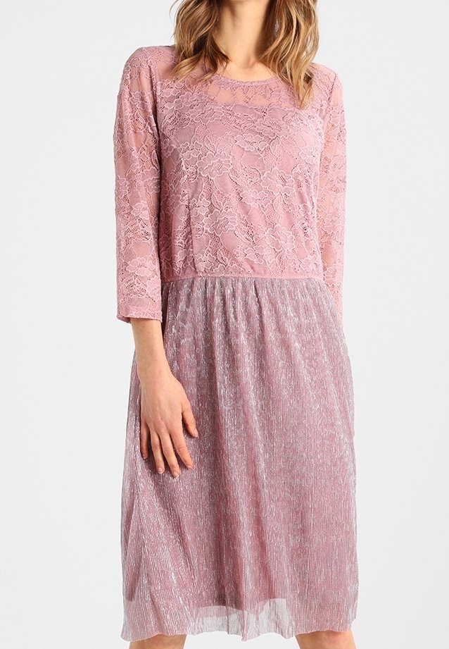 Femme portant une robe rose mi-longue avec un corsage en dentelle florale, des manches trois-quarts et une jupe plissée.