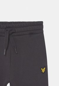 Mørkegrå sweatpants med elastisk talje, justerbar snøre og et lille gult broderet logo på venstre ben.