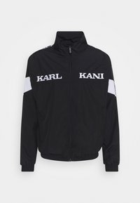 Black zip-up jacket made of lightweight material. Features white "KARL" and "KANI" logos, elastic cuffs, and a stand-up collar.