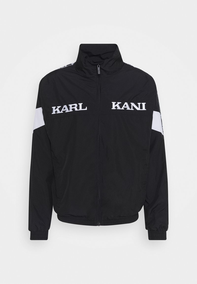 Black zip-up jacket made of lightweight material. Features white "KARL" and "KANI" logos, elastic cuffs, and a stand-up collar.