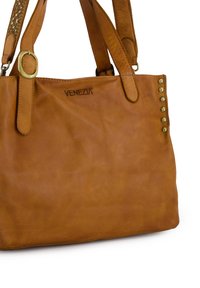 Braune Lederhandtasche mit glatter Textur, ausgestattet mit goldfarbenen Nieten auf einer Seite und einem eingprägten Logo auf der Vorderseite.