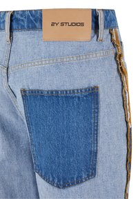 Light blue denim jeans featuring a large back pocket with contrasting blue fabric, brown stitching, and a leather tag labeled "2Y STUDIOS."