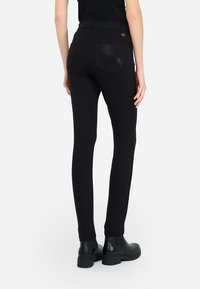 Pantalons noirs ajustés avec une texture lisse, une poche décorative en sequins et une taille haute. Assortis à des bottines noires.