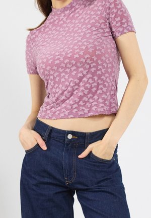 Haut violet à manches courtes avec un motif de papillon texturé, accompagné d'un jean en denim foncé taille haute avec des coutures contrastées.
