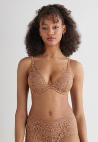 Kanten bh en bijpassende slipset in een zachte tan kleur. Bevat bloemmotieven, verstelbare banden en golvende randen op de slip.