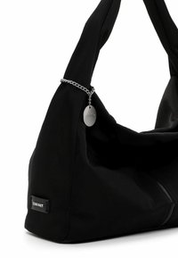 Juodos audinio peties krepšys su sidabrine grandinėle ir apvalia metaline etikete, pritvirtinta šalia rankenos, su mažu prekės ženklo ženklu apačioje.