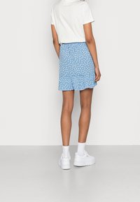 Jupe bleue à motif floral blanc, taille froncée, ourlet à volants. Associée à un t-shirt blanc et des baskets blanches avec des chaussettes.
